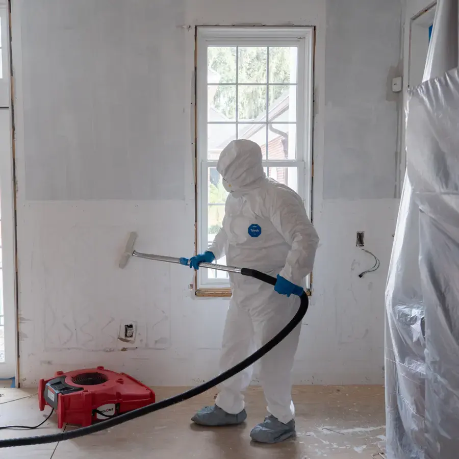 Mitigation technician in protective gear cleaning walls after a sewage backup